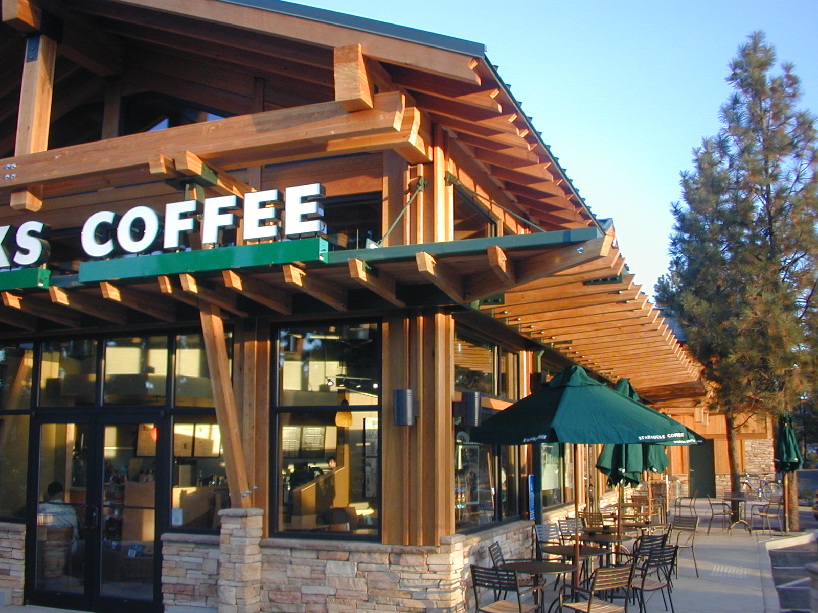 Wooden Starbucks location with large windows, green awnings, and outdoor seating.