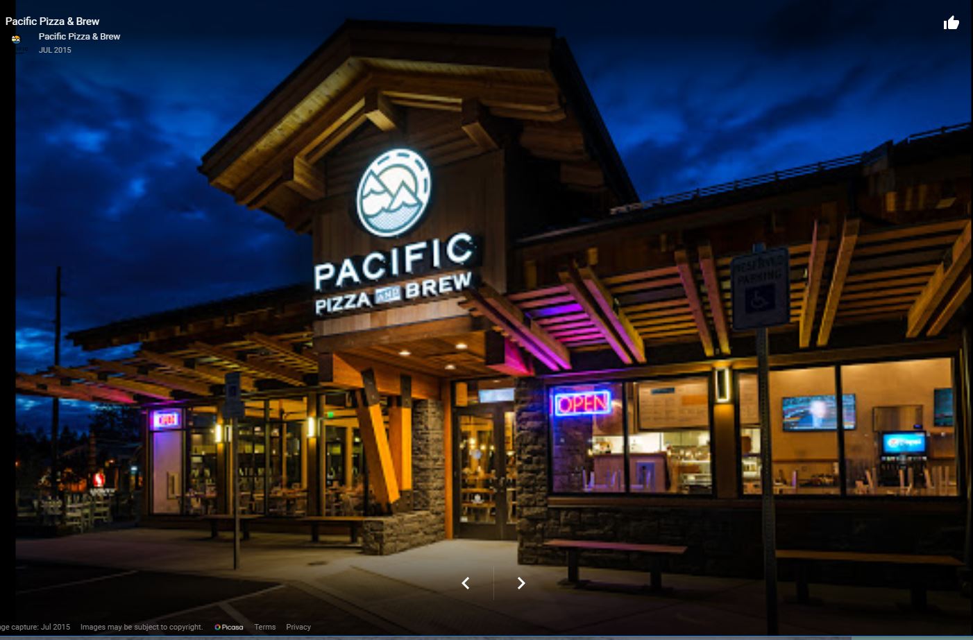 Pacific Pizza & Brew showcases its inviting exterior at night, featuring a brightly lit sign and an "OPEN" neon display, highlighting its welcoming atmosphere.