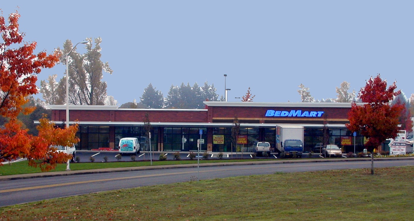 BedMart storefront featuring a large blue sign, surrounded by autumn trees.