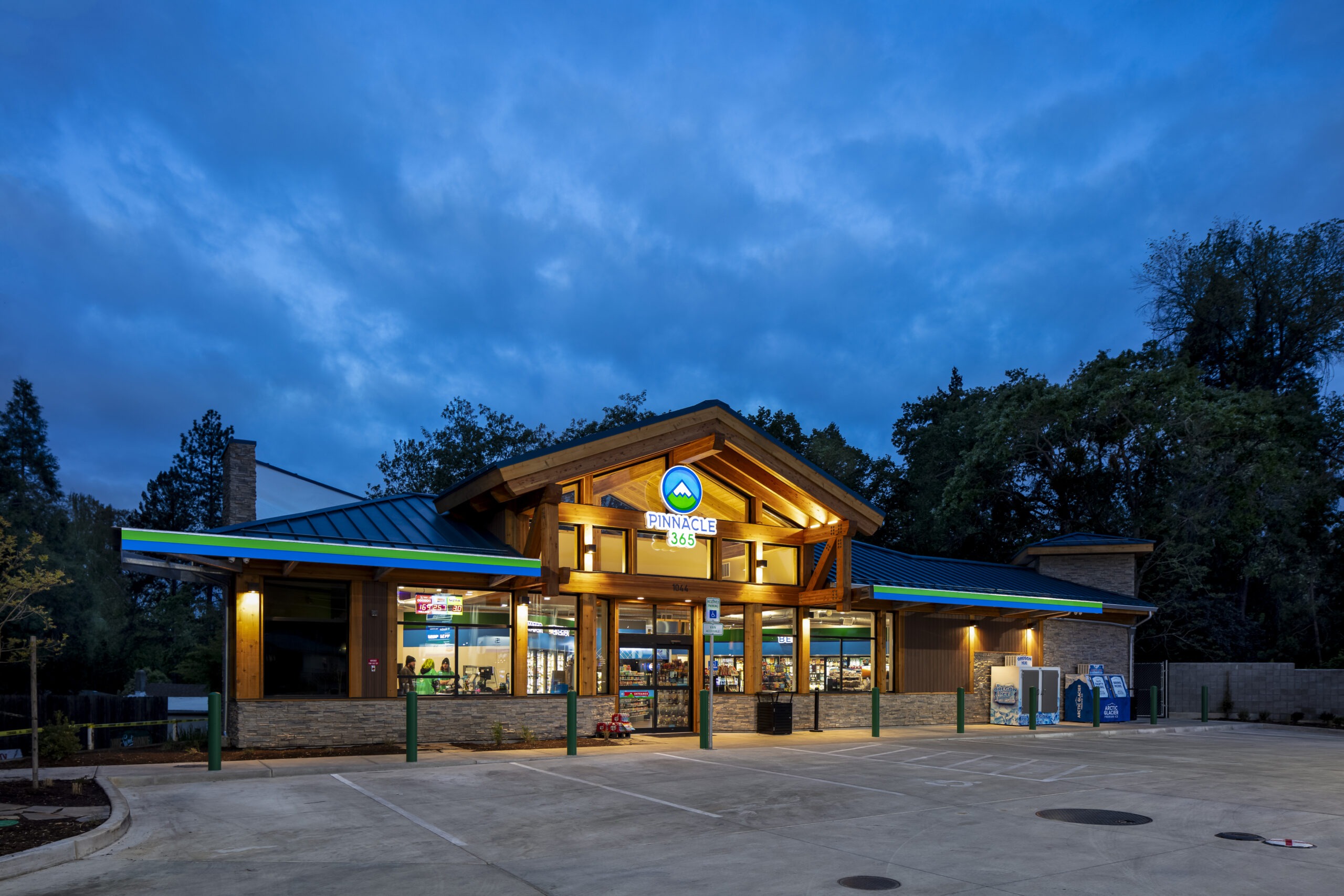 Pinnacle 365 convenience store at dusk, featuring a modern wooden structure, bright signage, and welcoming entrance, ideal for travelers.
