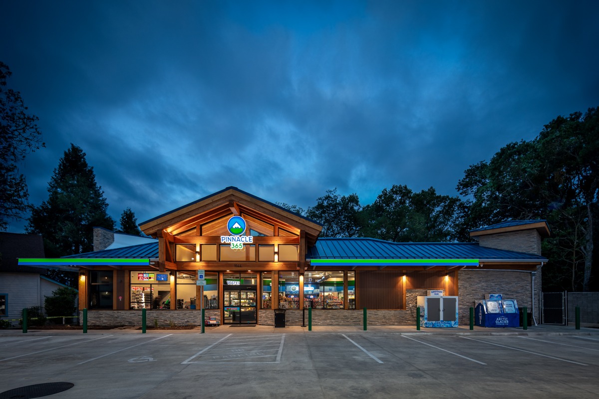 Pinnacle 365 convenience store exterior at dusk, featuring a wooden architecture, illuminated signage, and a well-lit parking area.